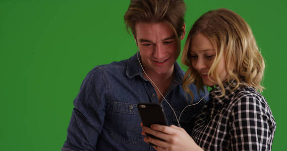 年轻夫妇的肖像使用手机一起听音乐在绿色屏幕上
