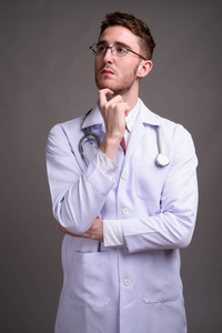 年轻英俊的男医生戴眼镜对灰色的背板