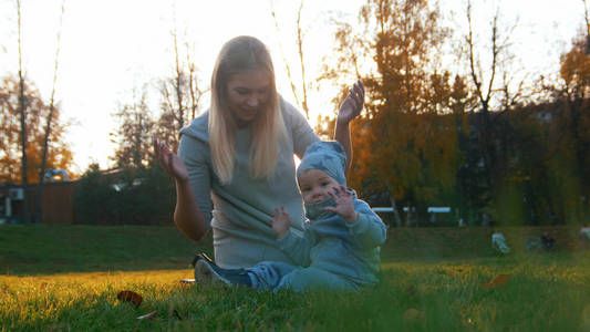 年轻的母亲和她的小宝宝在秋园玩耍。婴儿看着相机