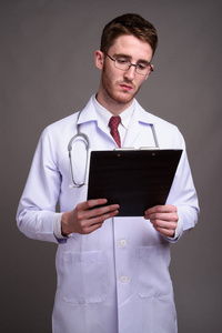 年轻英俊的男医生戴眼镜对灰色的背板