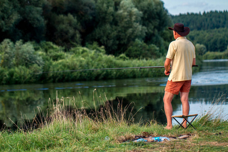 一个穿着短裤帽子和 t恤的渔夫正在湖岸上钓鱼。钓鱼爱好娱乐