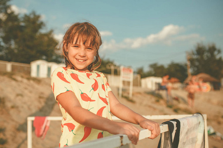 一个美丽的小女孩站在露台上, 靠在栅栏上, 在海滩上的肖像。暑假