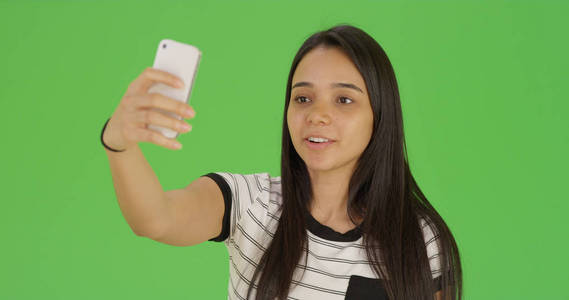可爱的女性青少年采取自拍与手机在绿色屏幕上