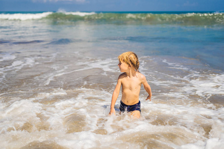 在异国情调的海岸线上在海浪中玩耍的小男孩