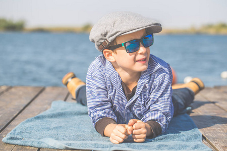 一个可爱的小男孩的肖像, 帽子和日光浴, 躺在河边, 享受美丽和阳光明媚的一天
