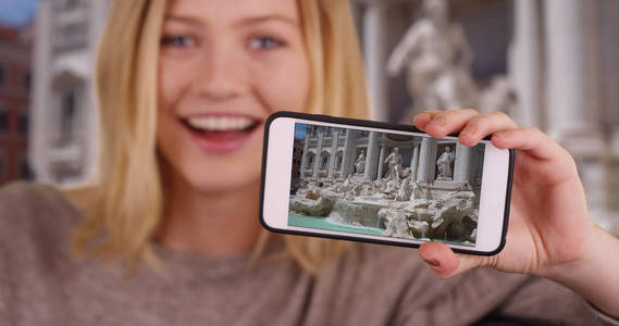 美丽的高加索女孩分享特雷维喷泉的智能手机图片