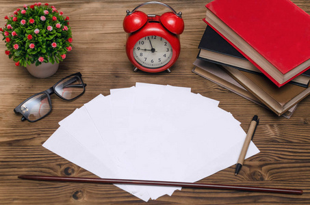 空白的试卷书籍学校指针眼镜和教室桌子上的红色闹钟。教育背景。测试工作的时间