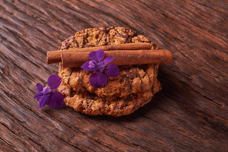 在木桌上浇水的巧克力糖浆饼干。可爱的组合与鲜花和肉桂棒。选择性对焦
