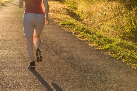美丽的运动的女人跑在乡间小路在日出光。美丽的女性跑户外在绿叶和绿色郊区