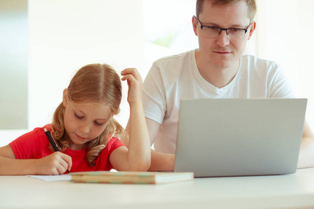 愉快的年轻的父亲有乐趣与他漂亮的小女儿在工作与笔记本电脑在现代家庭