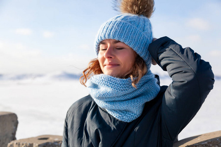 冬季背景下的肖像美女模特。美丽的现代年轻女子戴着蓝色针织帽享受, 在寒冷的海面上微笑着在冬天散步