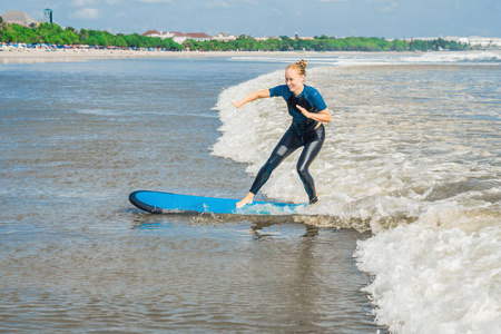 快乐的年轻女子在小海浪上与蓝色新手冲浪板一起冲浪