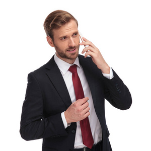 沉思的商人的画像在电话和看边, 当站立在白色背景时