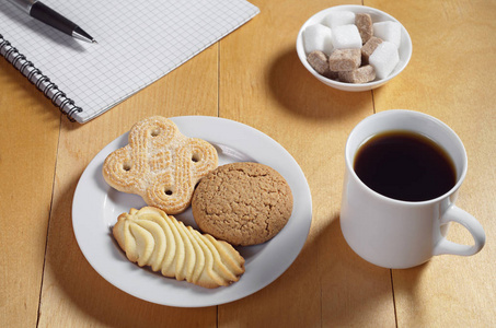 各种饼干咖啡和木桌上的钢笔笔记本