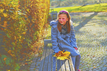 秋天, 小女孩穿着复古外套, 坐在公园的长椅上。小女孩拿着五颜六色的秋叶。秋天的概念。秋天的叶子