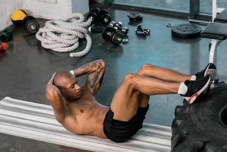 纹身非洲裔美国运动员做 abs 与腿在轮胎在健身房