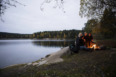年轻的朋友们在黄昏时坐在靠近湖边的篝火