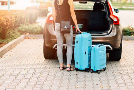 妇女装载二个蓝色塑料行李箱汽车后备箱。旅行准备