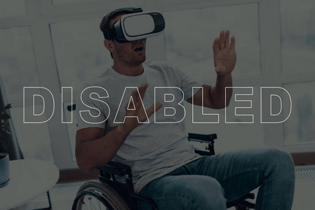 坐在轮椅上的残疾人。戴着虚拟现实眼镜的男人。人是指手的手势。男人很惊讶。成人褐发女郎男子. 人位于客厅。虚拟技术