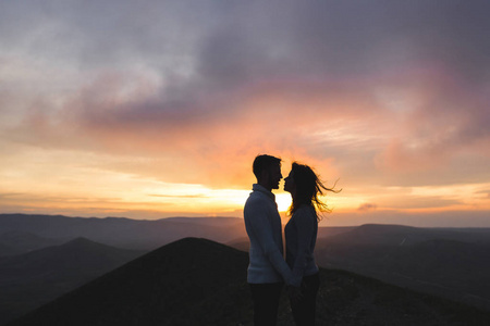 幸福的夫妇拥抱和亲吻在日落与惊人的山景。温暖的傍晚阳光