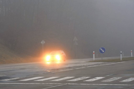 在雾中的汽车。恶劣的冬季天气和危险的汽车交通的道路上。轻型车辆在雾中