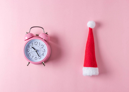 粉红色闹钟与圣诞老人帽子在柔和的粉红色的背景。最小的圣诞节概念