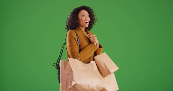 愉快的黑色女性购物者与购物袋看起来兴奋在绿色屏幕上