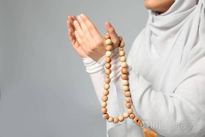 年轻的穆斯林妇女与念珠祈祷在轻的背景, 特写镜头