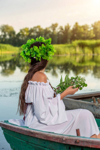 穿着白色复古礼服的黑发长的仙女, 坐在河中央的一条船上