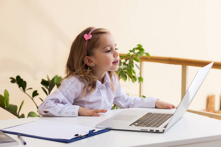 漂亮的小女孩正坐在表与笔记本电脑