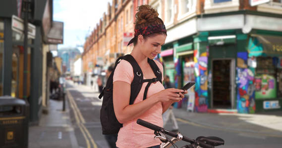 漂亮的白人妇女检查电话, 而她的自行车骑在伦敦各地休息