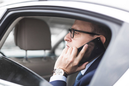 年轻的成功商人坐在一辆精英汽车的后座上打电话, 参加会谈和商务会议