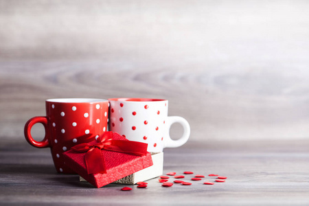 一对白色和红色的杯子, 由红心装饰, 并在木桌上的盒子里赠送礼物。情人节庆祝概念。复制空间