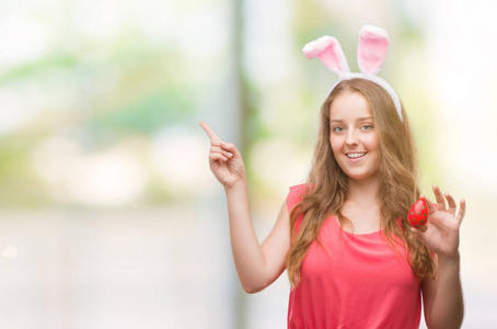 年轻的金发碧眼的女人穿着复活节兔子耳朵非常高兴用手和手指指向一边