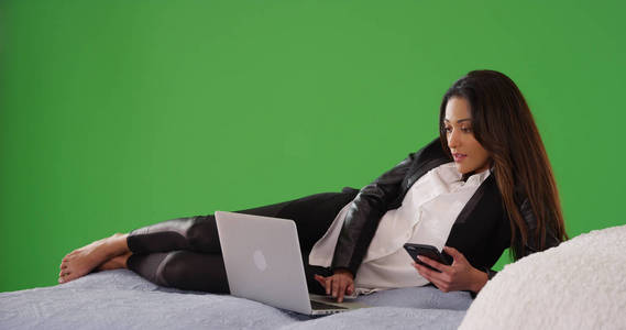 成功的拉丁女商人躺在床上工作的笔记本电脑上的绿色屏幕