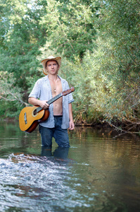 年轻男子在一个开放的衬衫和一个牛仔帽用吉他在他的手中是涉水过河