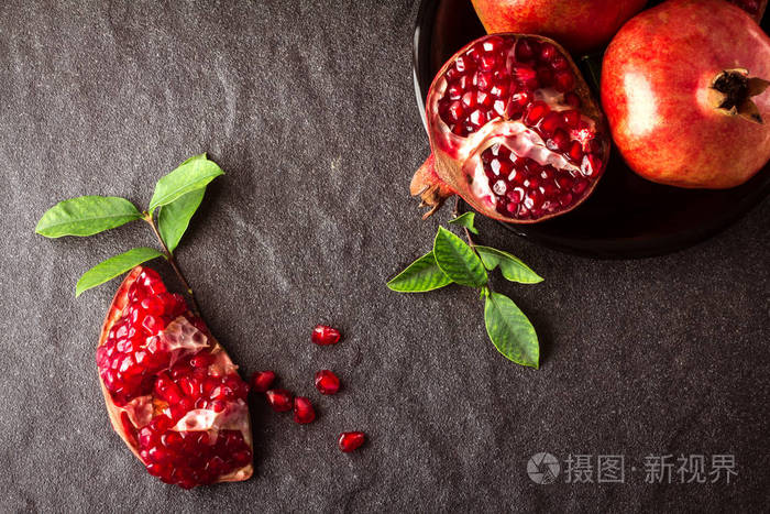 新鲜红石榴和种子与树叶黑色的石头