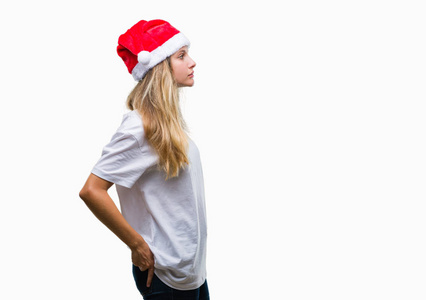年轻美丽的金发女子戴着圣诞节帽子在孤立的背景寻找侧, 放松的轮廓姿势与自然脸与自信的微笑