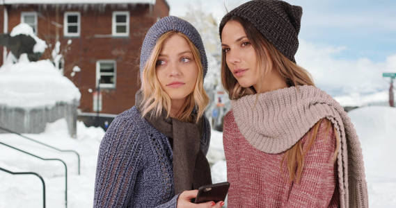 在雪山的小区里, 两个女孩穿着智能手机过冬