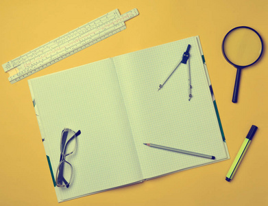 一个大笔记本的笔记和绘图文具对象的学生在黄色背景。标尺标记铅笔放大镜罗盘眼镜。顶视图