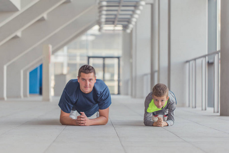 小男孩和他的教练一起在体育中心做俯卧撑练习。父子之间的时光, 并引领健康的生活方式。一起锻炼健身日。运动的家庭概念。积极的生活方