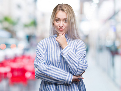 年轻的金发女人在孤立的背景下, 看着自信的相机与交叉的手臂和手举起下巴。积极思考