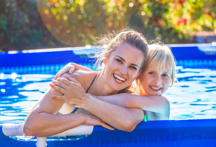 微笑活动的母亲和孩子在游泳池里拥抱