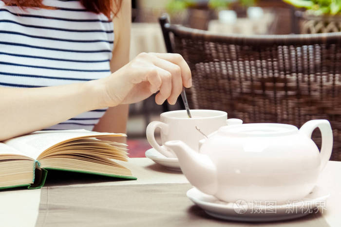年轻漂亮的女孩在户外咖啡馆里看书,喝咖啡
