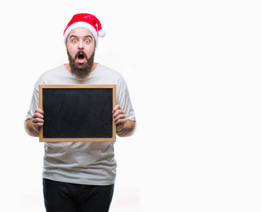 年轻的高加索嬉皮士男子戴着圣诞帽, 拿着黑板在孤立的背景吓得惊心动魄的一张惊讶的脸, 害怕和兴奋与恐惧的表情