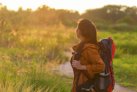 亚洲徒步者背着背包走在国家公园里。女游客去野营在草甸森林, 日落背景。旅游理念