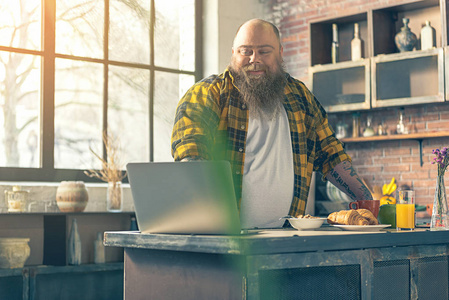 开朗的男性胖子娱乐性与厨房的笔记本电脑