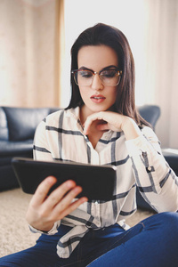在眼镜上平板电脑在家里读书的年轻聪明的女人