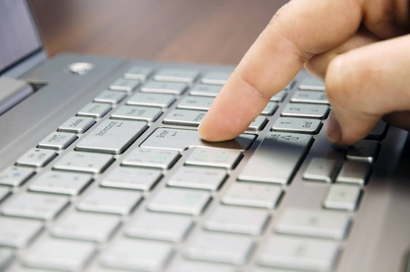 用一根手指的手的特写视图躺在木垫模糊的银色键盘笔记本电脑上按 Enter 键