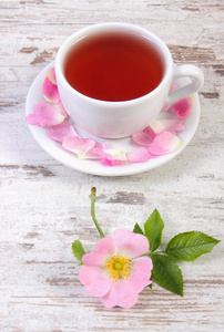杯热茶和仿古木制背景上的野生玫瑰花朵